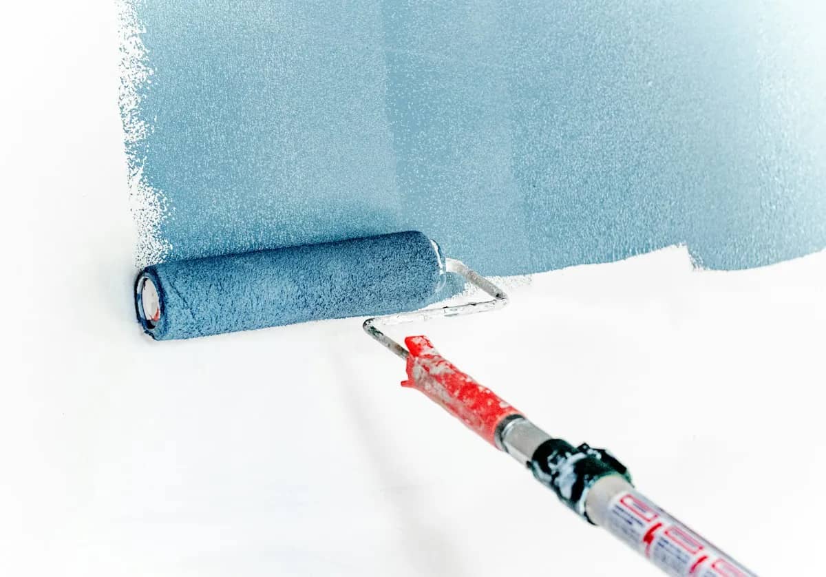 Rolo de pintura aplicando tinta azul em uma parede branca